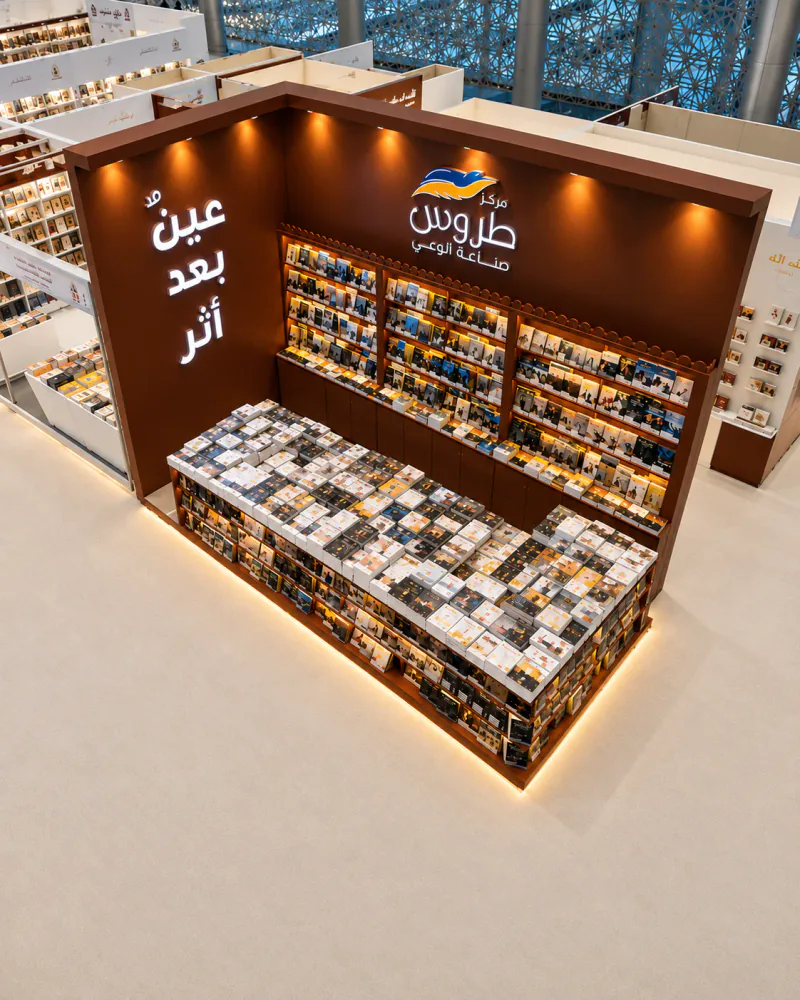 Elevated photograph of the Torous Publishing booth, showing its brown walls, illuminated Arabic branding, bookshelves and front book display