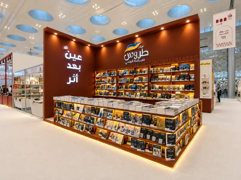 Photograph of the Torous Publishing book-fair stand with brown walls, illuminated bookshelves and the blue-and-gold feather emblem