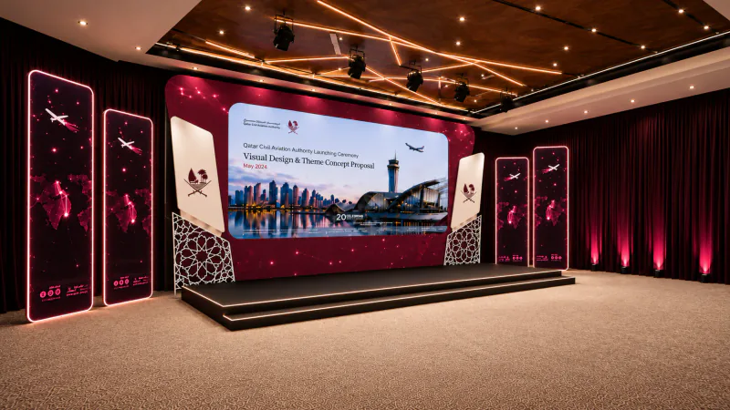 Enhanced angled render of the QCAA strategy launch stage with maroon screens, Qatar emblems and warm ceiling lights